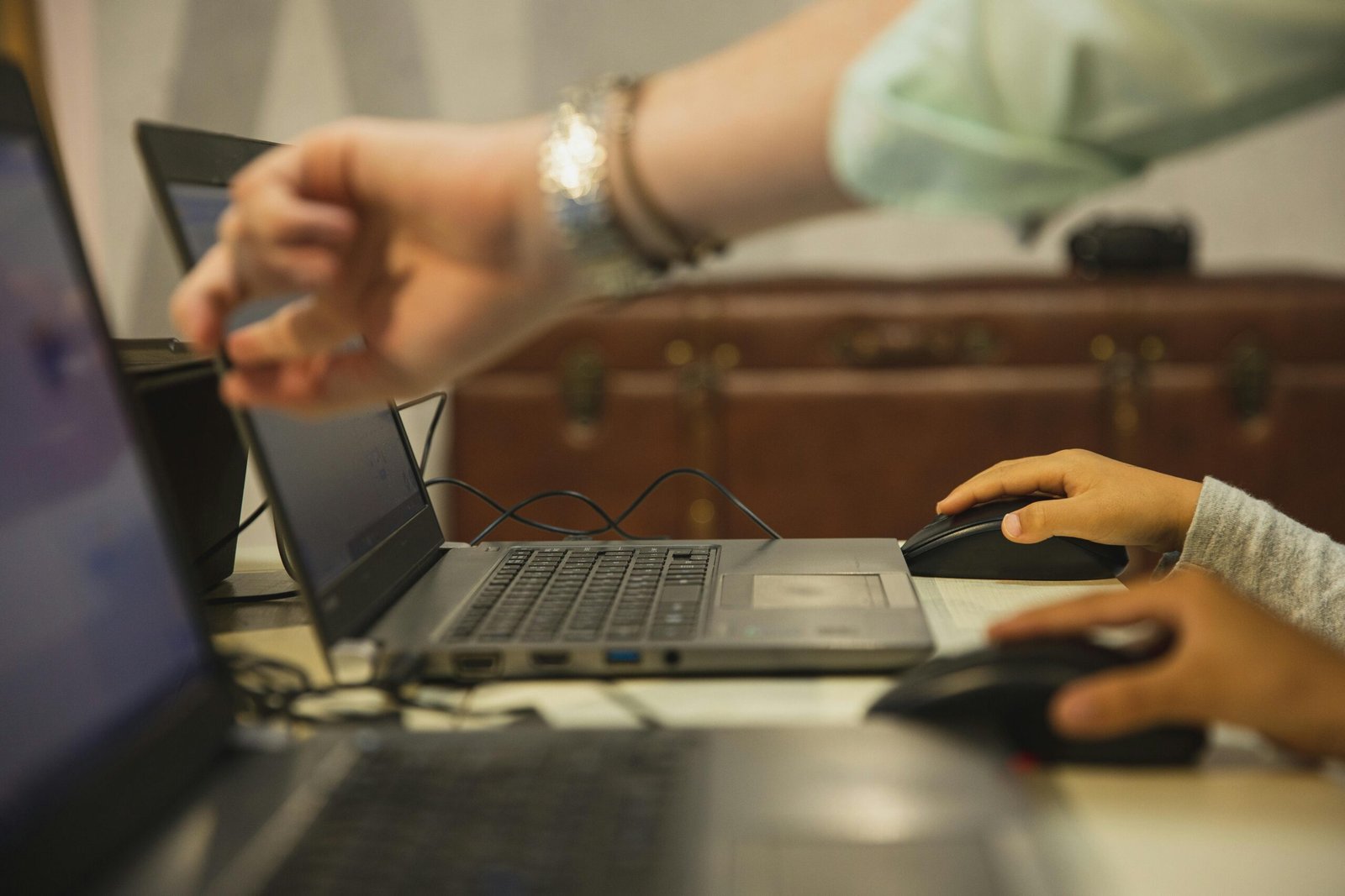 Crop anonymous female teacher pointing at netbook screen near schoolchildren touching mouses at desk in classroom